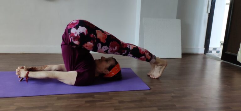 "Person in yoga Halasana pose, lying on their back with legs extended over the head, feet touching the ground behind, arms extended flat on the floor, a calm and peaceful yoga environment with soft lighting."